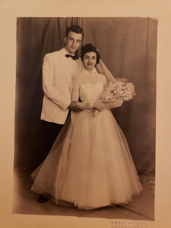 Couple poses together in formal wedding attire with a bouquet in a studio from the past era.