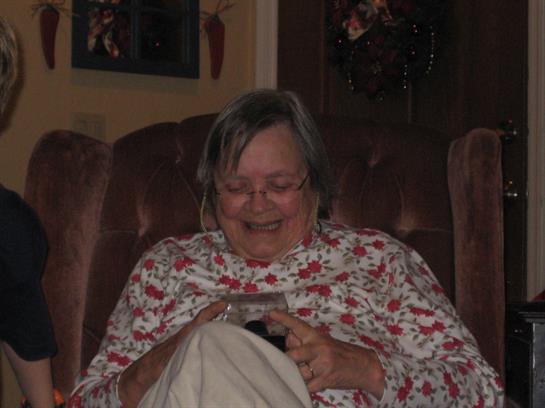 A joyful elderly woman sits comfortably at home, engaged with her mobile device during the evening.