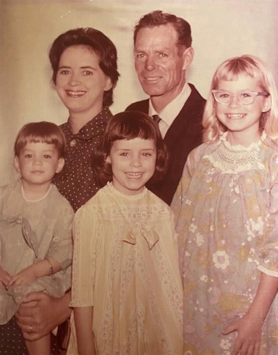 A happy family in vintage clothing stands together, smiling warmly.