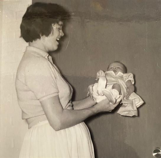 A woman expresses joy while holding her newborn baby in a charming indoor space.