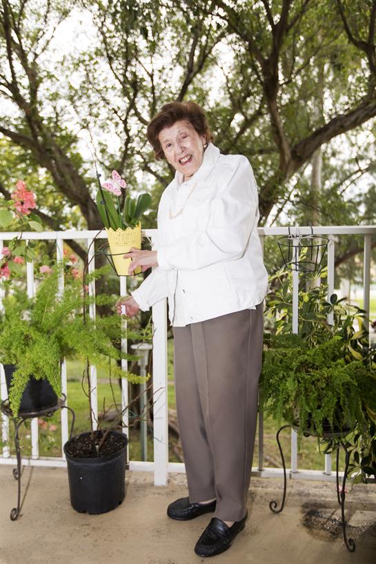A joyful woman tends to her balcony garden, engaging with colorful flowers and lush greenery.