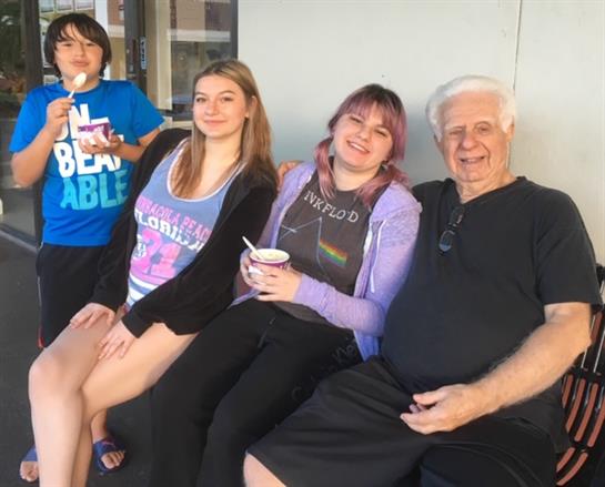 Four family members relax on a bench, enjoying ice cream on a warm afternoon.