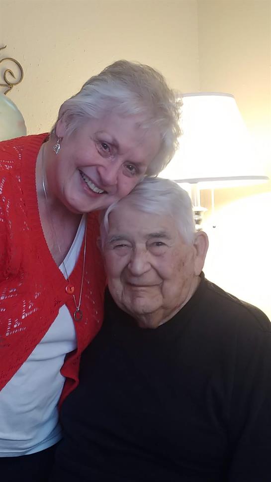 Smiling elderly couple embraces each other, enjoying a joyful moment at home with family.
