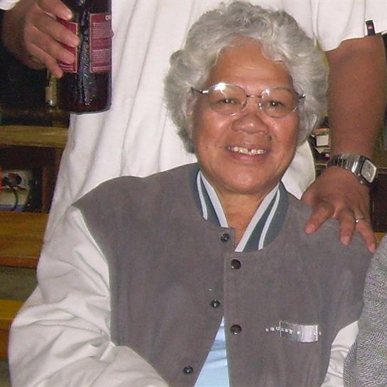 A woman with curly gray hair is smiling in a casual atmosphere while enjoying time with friends.