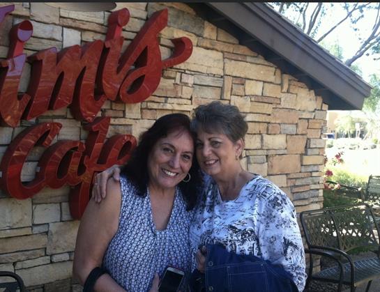Two women share a friendly smile outside a charming cafe adorned with stone walls.