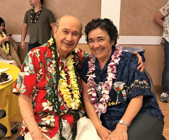Two smiling individuals in colorful outfits are enjoying a joyful moment at a celebration.