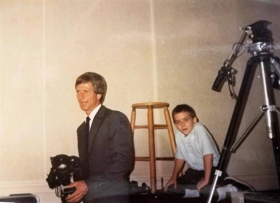A man with a camera prepares for a photo shoot while a boy waits on a stool.