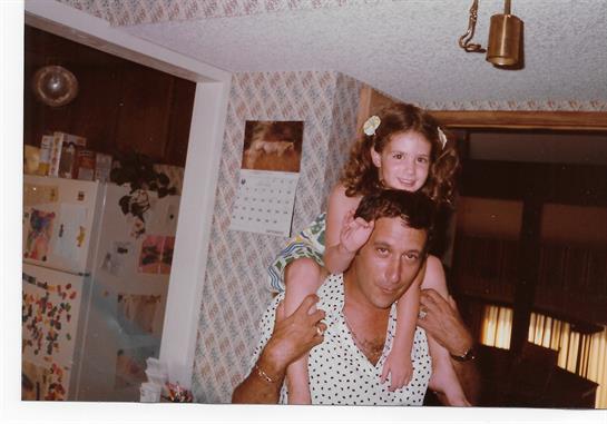 A joyful girl sits on her father's shoulders, smiling brightly in their warm home.