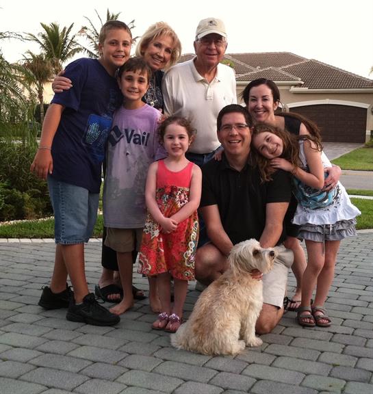 A happy family enjoys a warm evening outdoors in their yard with kids and a dog.