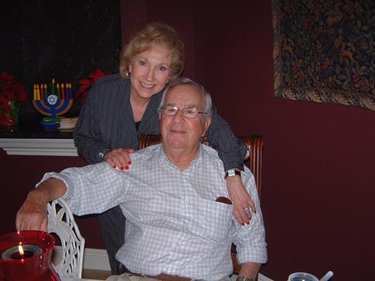 Two people share a joyful moment in a warmly decorated dining space surrounded by family.