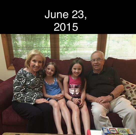 Grandparents pose with their two granddaughters on a couch in a cozy living room on a summer day.