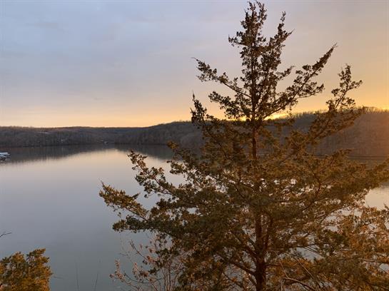 Golden hues illuminate the lake as the sun sets behind the hills, creating a tranquil atmosphere.