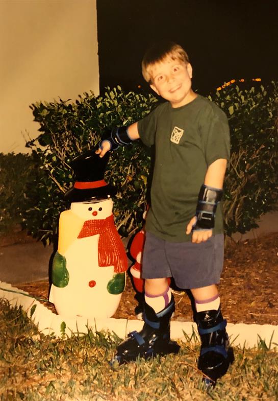 A boy enjoys rollerblading and poses with a colorful snowman decoration in a yard.