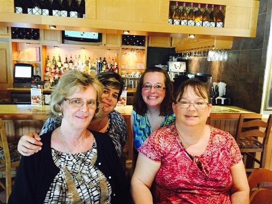 Four women smile and pose together at a bar, enjoying their time in a vibrant restaurant.