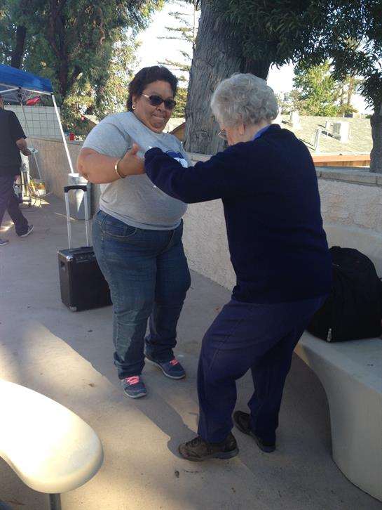 Two women dance joyfully in a park during a festive community gathering.