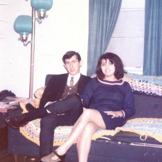 Couple relaxes on a couch, surrounded by colorful curtains and vintage lamps.