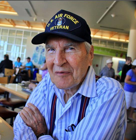 An elderly veteran engages with visitors at a community center during a social gathering.