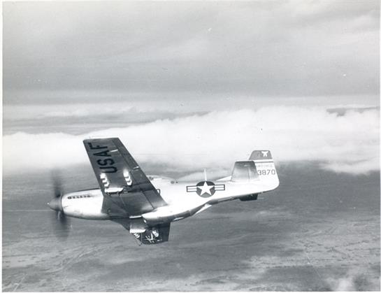 A vintage military airplane flies above the clouds, showcasing its sleek design and insignia.