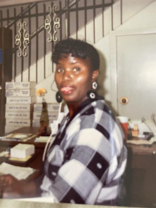 A woman is seated at a reception desk, engaging with visitors while wearing trendy apparel.