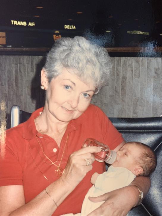 An elderly woman lovingly feeds a newborn baby while smiling in a warm, inviting atmosphere.