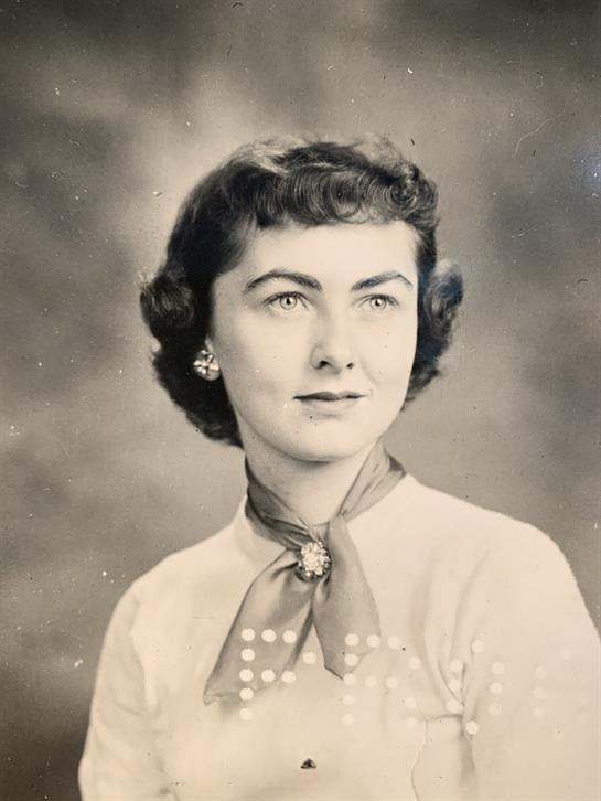 A young woman poses for a classic portrait wearing a scarf, looking thoughtfully at the camera.