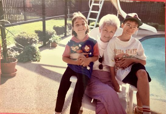 Children and their grandmother smile while sitting together outdoors in a sunny backyard.