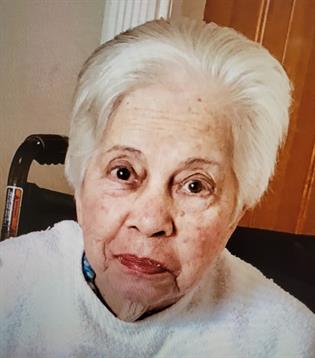 An elderly woman with white hair has a kind expression, radiating warmth indoors.