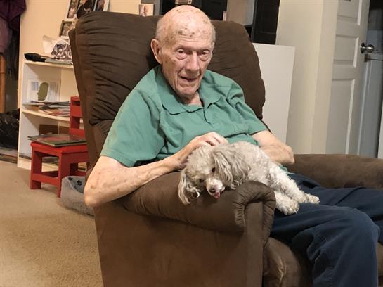 Elderly man relaxes in a chair with a small dog on his lap, enjoying companionship.