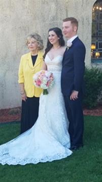 A bride in white poses with her groom and a woman in a yellow jacket at the wedding.