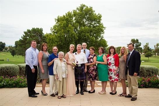 A family gathers outdoors, smiling and elegantly dressed to celebrate a wedding.