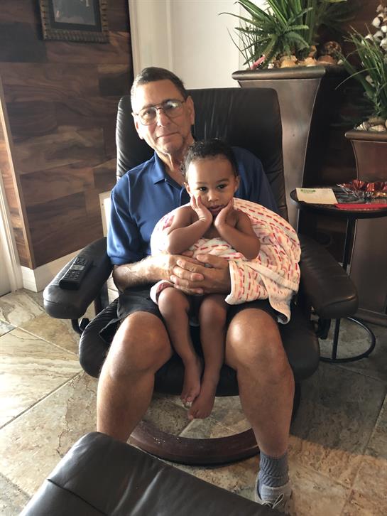 An elderly man embraces a baby, providing a warm and joyful atmosphere in a comfortable setting.