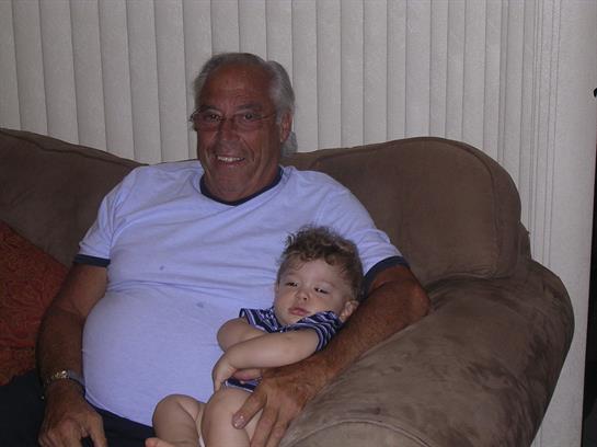 An elderly man and a young child share a warm, affectionate moment while sitting on a couch.