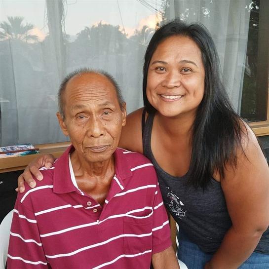 A woman smiles brightly next to an elderly man in a casual gathering at sunset.