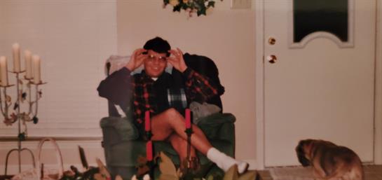 A person relaxes in a chair, playfully adjusting their sunglasses in a warm room.