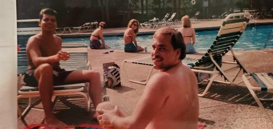 Group of individuals relaxes poolside while enjoying the warm sunshine and socializing.