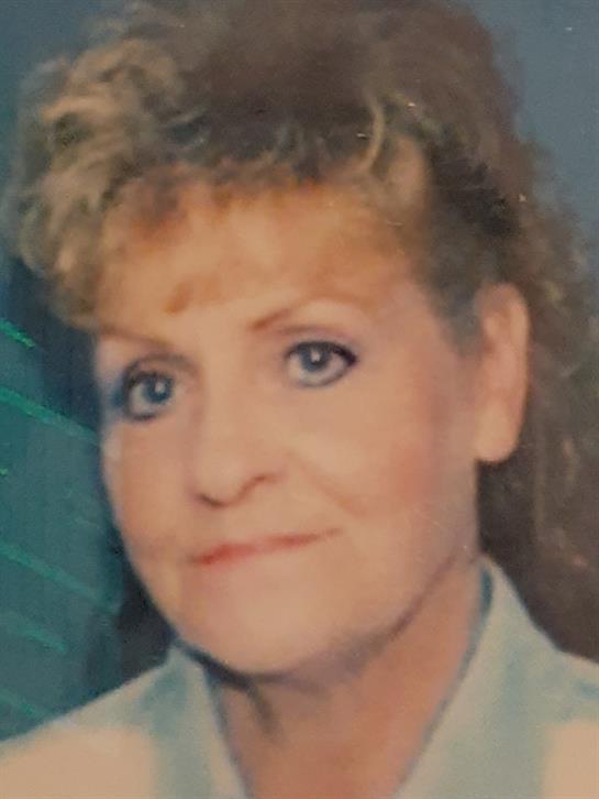 A woman with curly hair wears a light outfit and smiles gently in a calm environment.