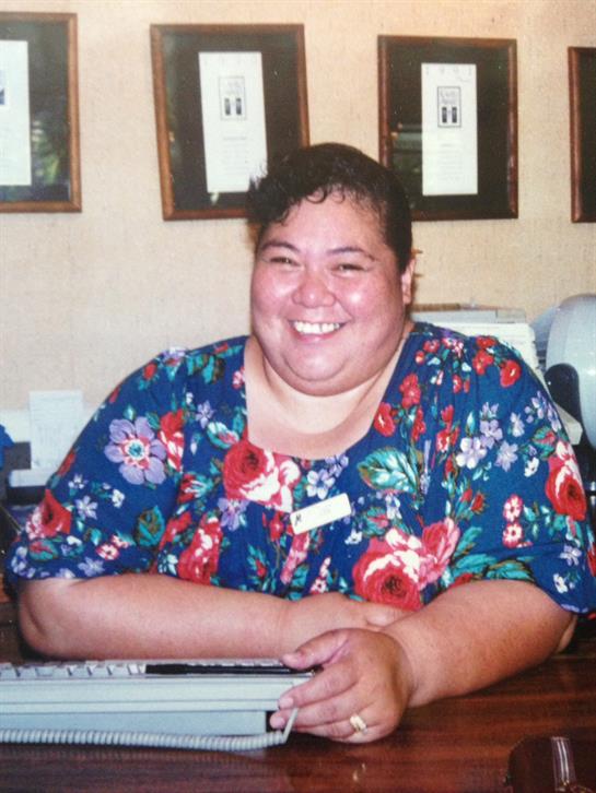A cheerful receptionist with curly hair sits at her desk, surrounded by framed pictures.