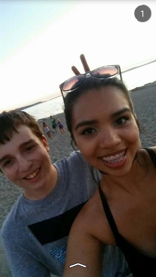 Two friends smile and pose at the beach during a summer evening, capturing joyful moments.