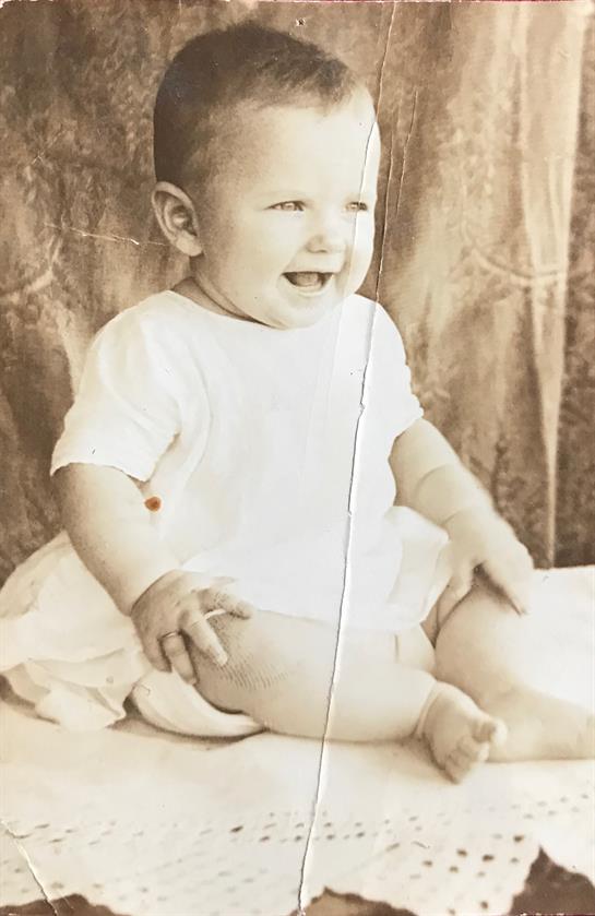A smiling baby sits comfortably on a soft surface, exuding joy in a vintage style portrait.