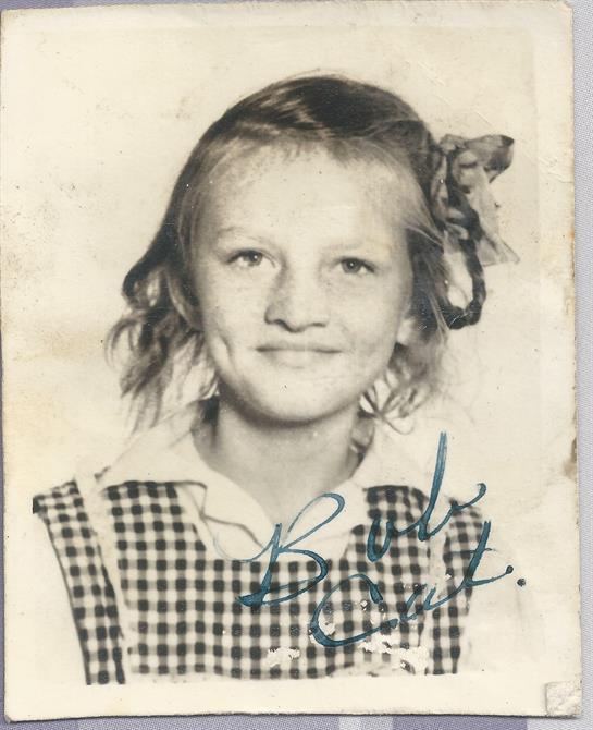 A young girl in a checkered dress and hair ribbon radiates childhood innocence with her smile.
