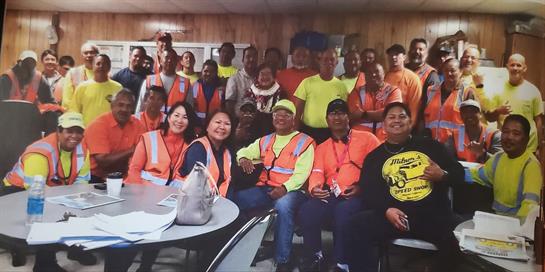 Group of community workers in bright vests gather joyfully, showcasing teamwork and friendship.