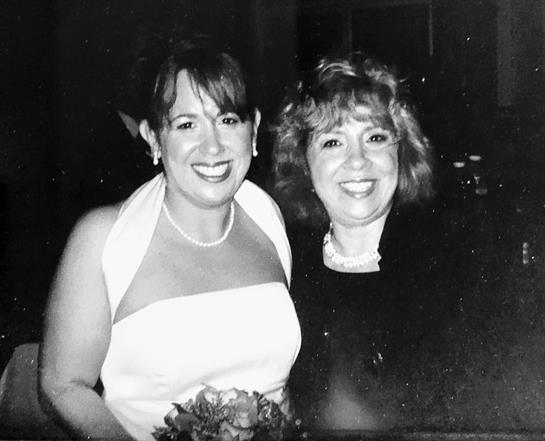 Two women smiling joyfully while wearing formal dresses and holding a bouquet of flowers.