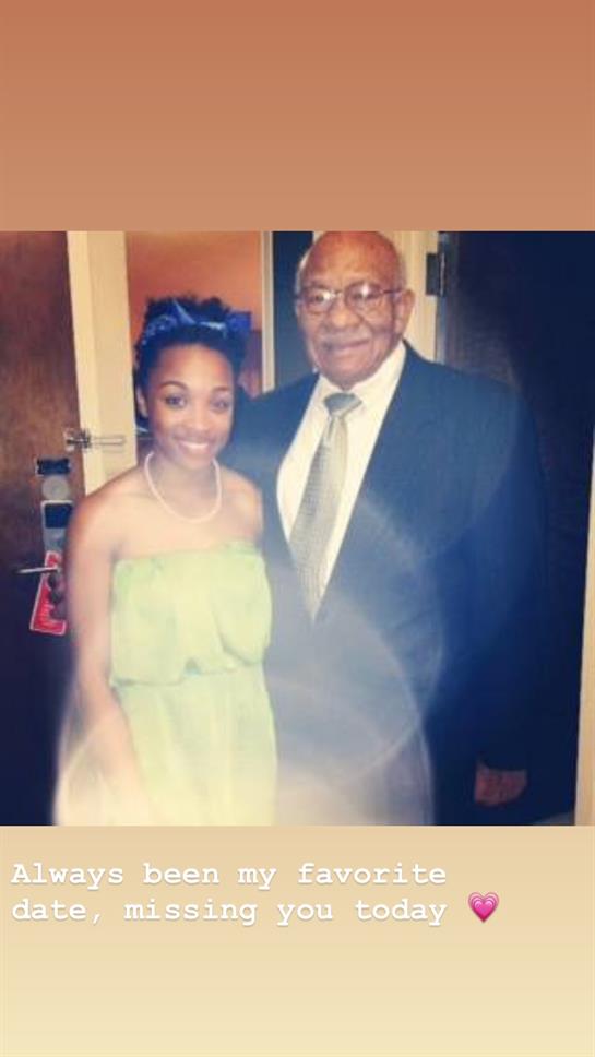 A young woman in a green dress poses joyfully with an older man in formal attire, smiling warmly.