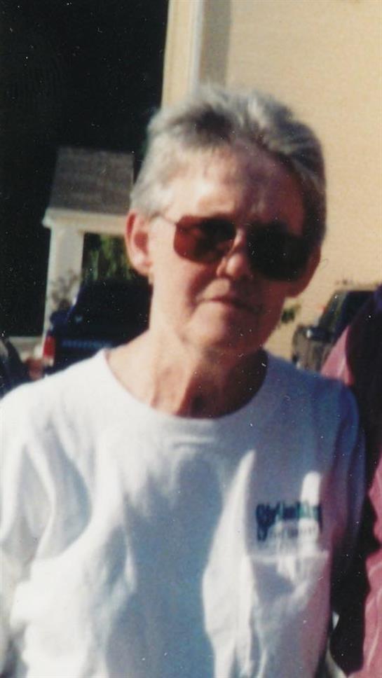 An elderly woman with silver hair enjoys a warm day outdoors while wearing sunglasses.