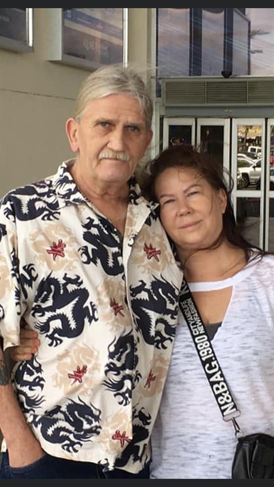 A smiling couple stands closely together outside a shopping center, enjoying their time.