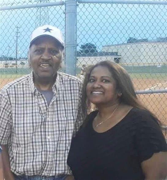Couple stands closely together, smiling, at a sports field as daylight fades.