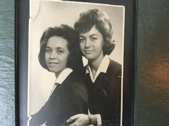 Two women stand closely together, displaying fashionable hairstyles and attire in a studio setting.