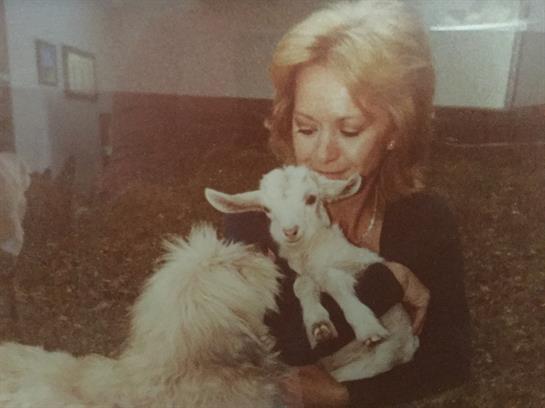 A woman lovingly holds a baby goat while a friendly dog looks on, creating a warm atmosphere.