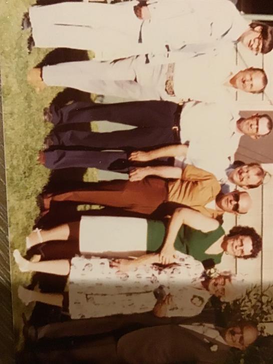 A joyful gathering of family members poses together in a green backyard on a sunny day.