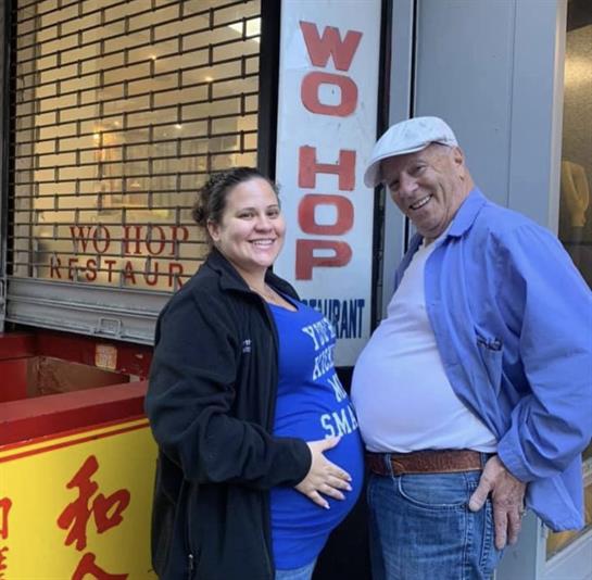A happy couple stands together, showcasing a playful moment near a vibrant restaurant entrance.